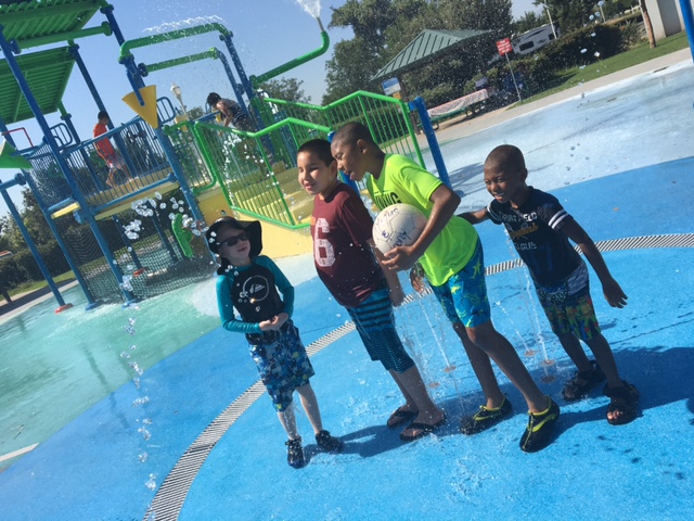 Four boys standing in a fountain, one holding a soccer ball