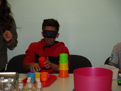 A child is blindfolded and asked to position plastic cups as if he were blind