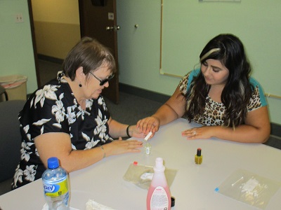 Nancy is showing Teresa how to paint your nails when you are blind.