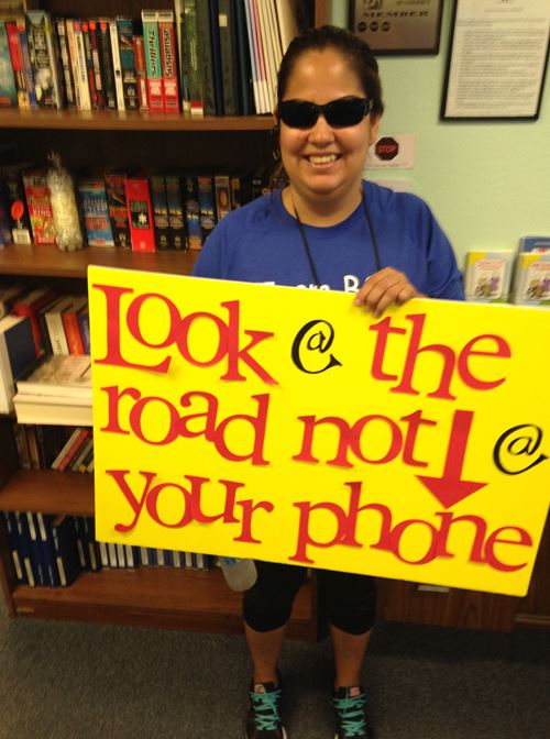 Priscilla holding a sign that says to look at the road not your phone