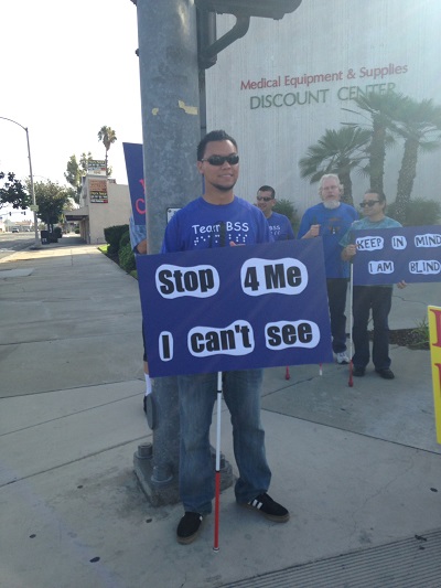 Feliciano standing on the street holding a sign that says stop for me I can't see