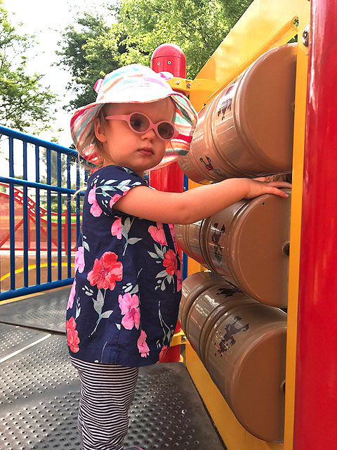 A little girl is playing with some of the sensory attractions on a wall