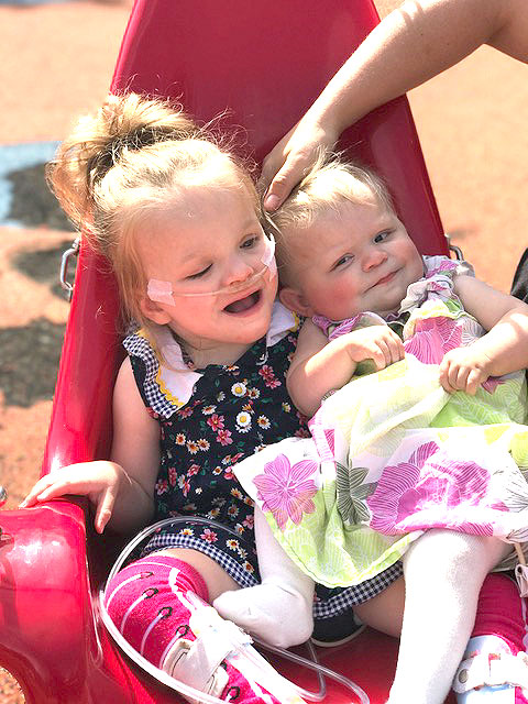 These two children are smiling while sitting on a swing together