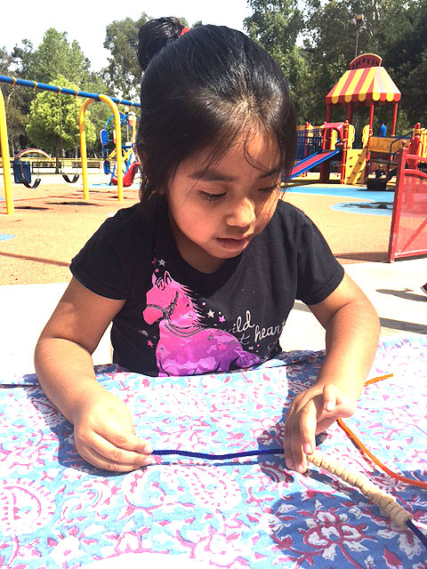 A child is playing with tactile beads that he is putting on a fuzzy pipe cleaner