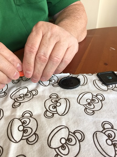 An elderly woman is sewing buttons on to some fabric.