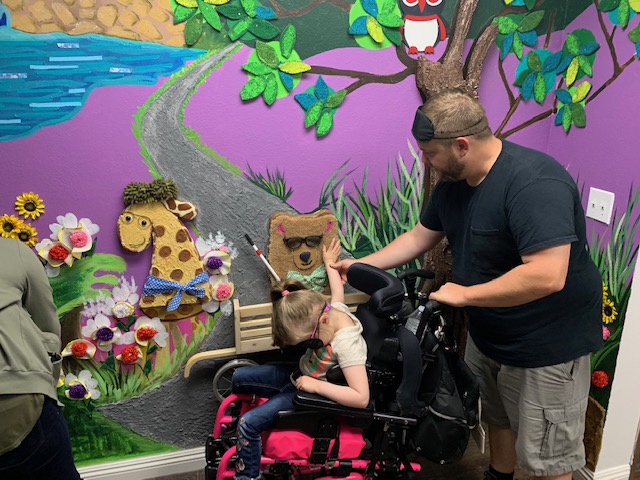 a power chair bound girl feeling the bear on our tactile mural